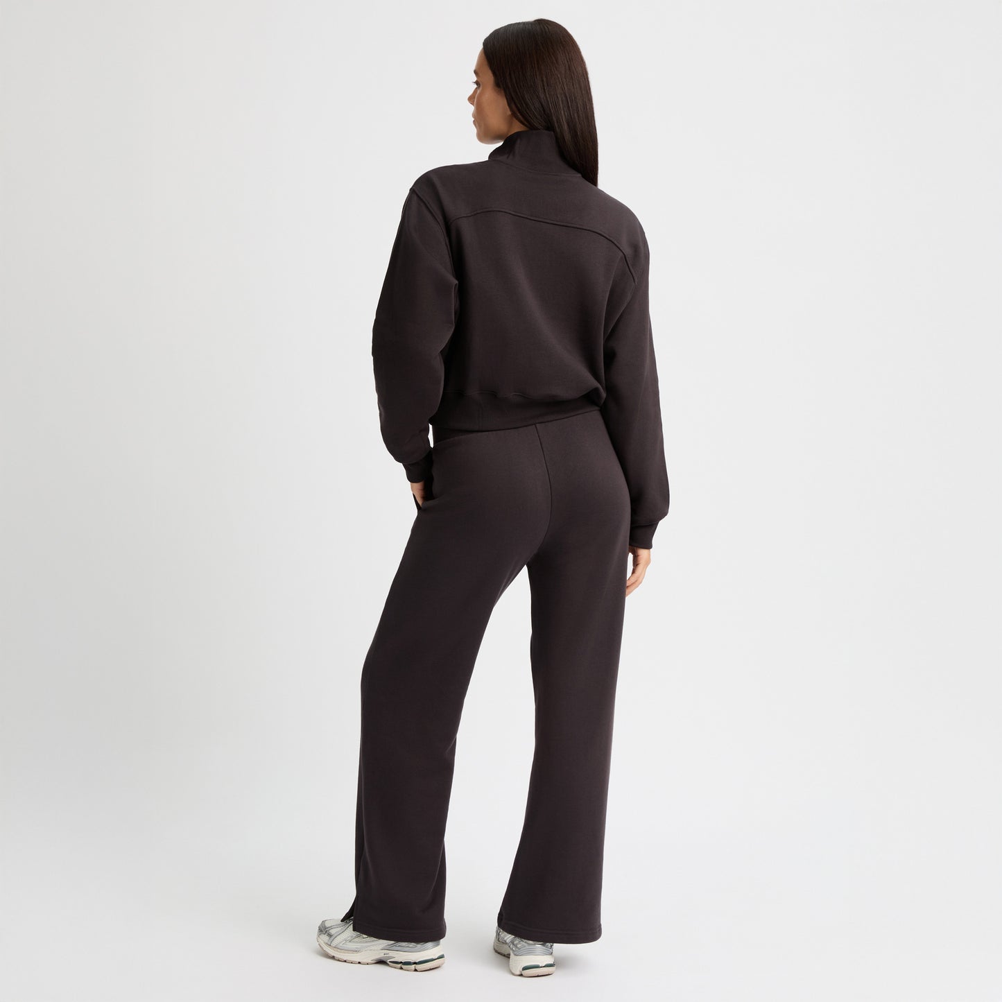 A woman in a black tracksuit and sneakers stands against a white background. She's wearing Rohnisch's Soft Sweat Wide Pants, combining style and comfort effortlessly.