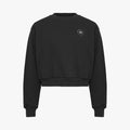 The Soft Sweatshirt by Rohnisch is a black cropped design with long sleeves, made from recycled fabric. It showcases the brand's signature white logo embroidery on the upper left chest.