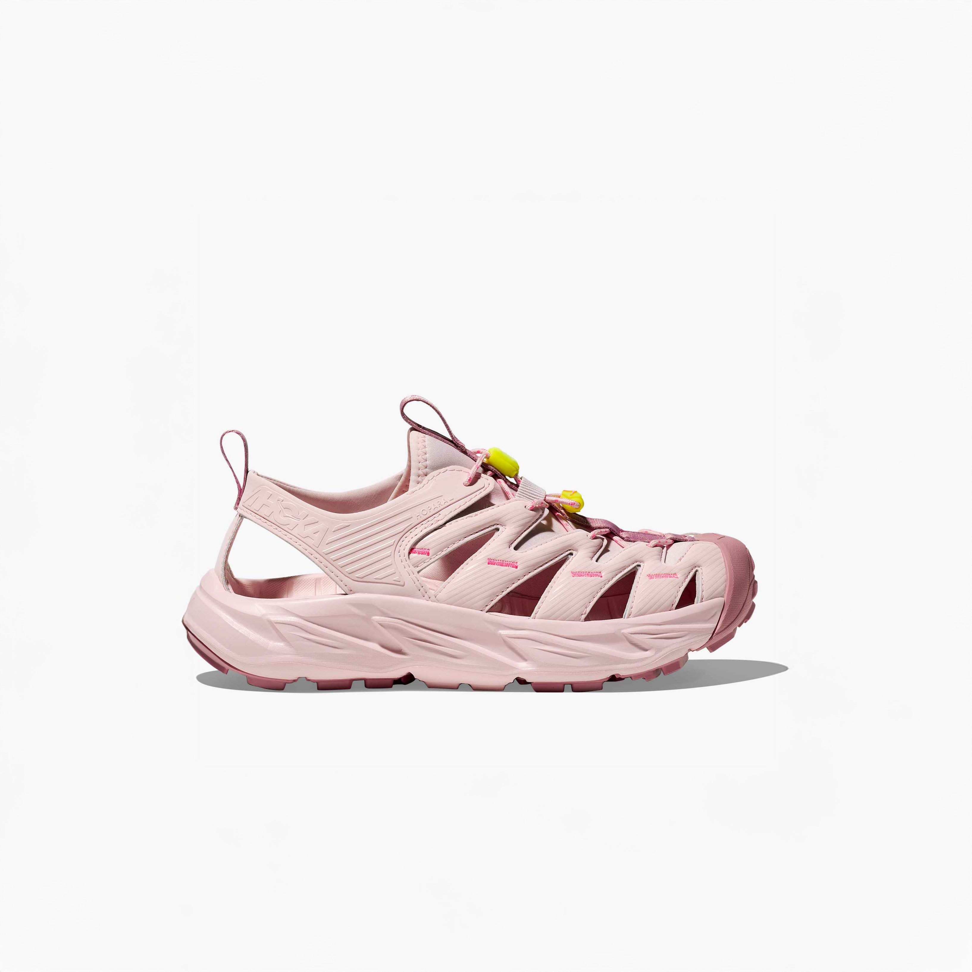 The Hoka U Hopara sandal in Rose Tea/Neon Rose features cut-out sides, a thick textured sole, and yellow Quick Lace toggle laces, shown on a plain white background.