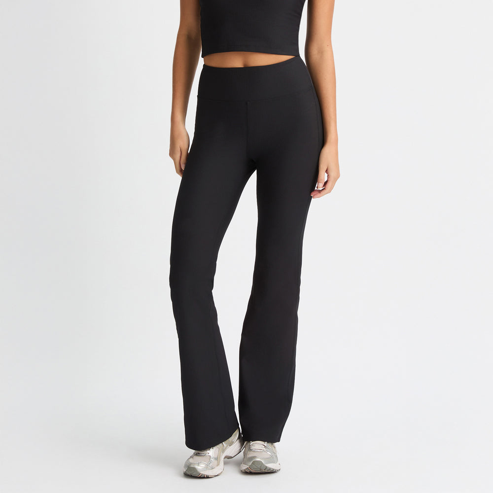 A person wearing a black crop top and Rohnisch's Ribbed Flair High Waist Tights made from recycled polyester, complemented by silver sneakers, stands against a white background.
