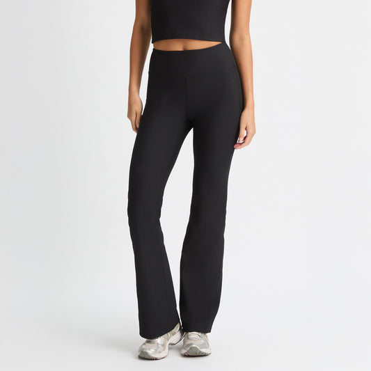 A person wearing a black crop top and Rohnisch's Ribbed Flair High Waist Tights made from recycled polyester, complemented by silver sneakers, stands against a white background.