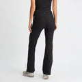 A person in black Ribbed Flair High Waist Tights by Rohnisch, paired with a matching top and sneakers, stands facing away against a white backdrop. The elegant flair of the recycled polyester fabric enhances their athletic look.