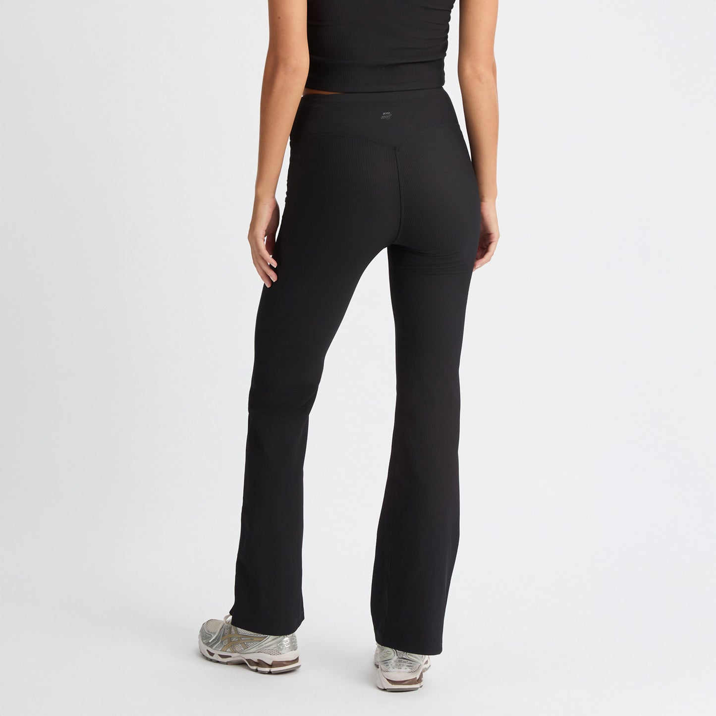 A person in black Ribbed Flair High Waist Tights by Rohnisch, paired with a matching top and sneakers, stands facing away against a white backdrop. The elegant flair of the recycled polyester fabric enhances their athletic look.