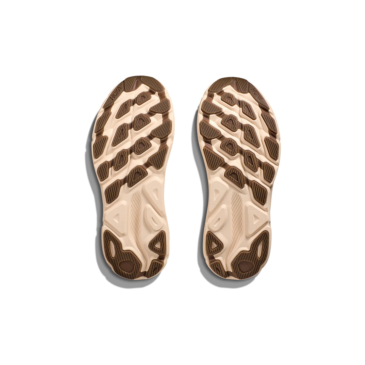 The Hoka M Clifton 9 in Wheat/Shifting Sand features beige and brown athletic soles designed for cushioning and a responsive toe-off, shown from the bottom against a white background. Inspired by the comfort of Clifton 9.