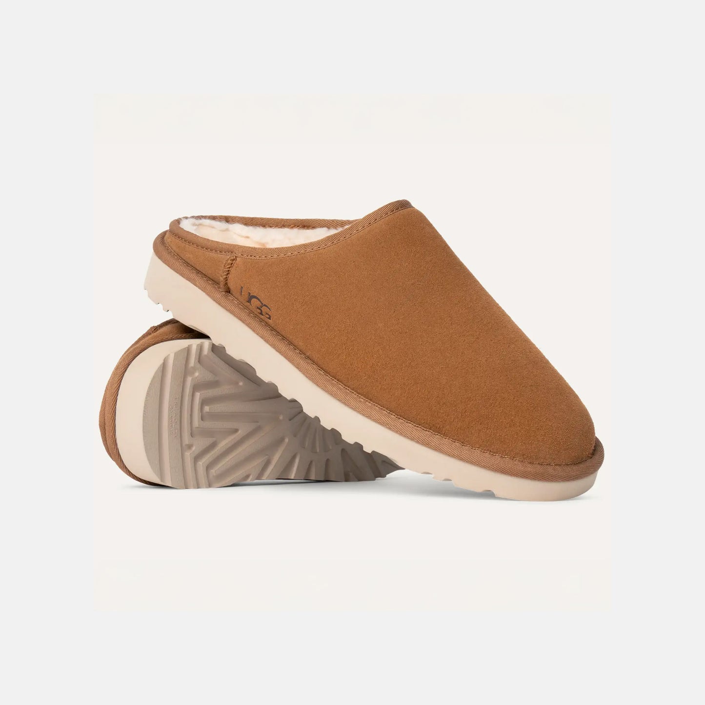 The Ugg M Classic Slip-On, featuring a plush suede finish with a textured sole and white lining, rests against a plain background.