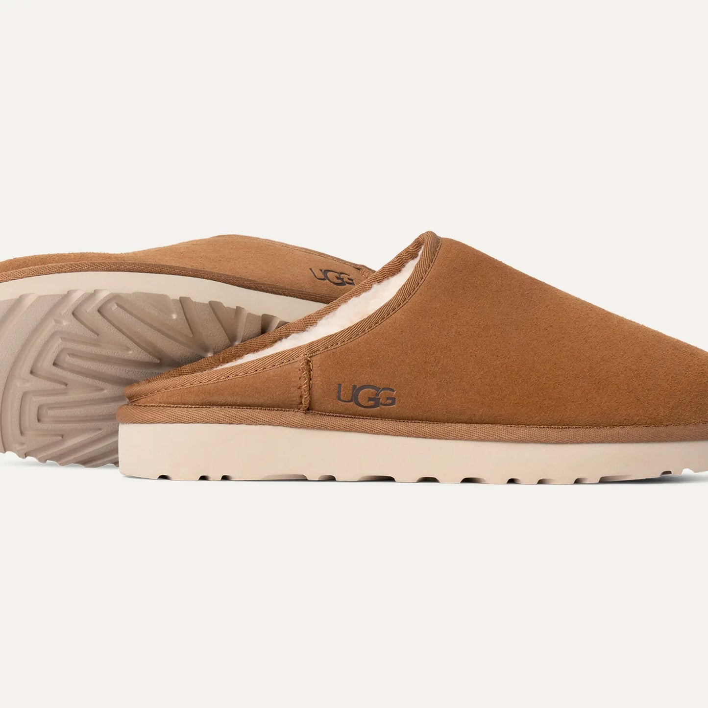 Tan M Classic Slip-On slippers by Ugg, made of soft sheepskin with a plush interior lining and textured rubber soles, displayed side by side.