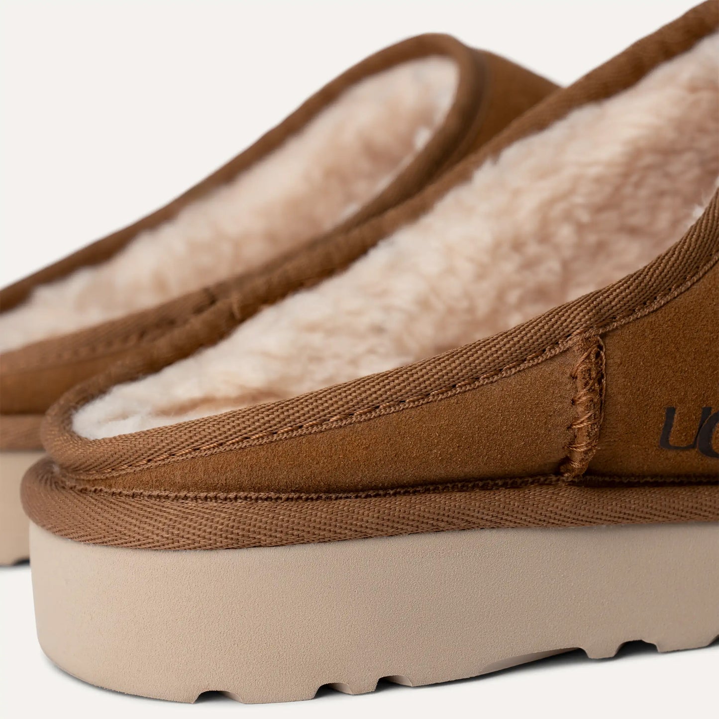 Close-up of Ugg's M Classic Slip-On in brown suede, showcasing plush fleece lining, thick soles, and UGGplush™ comfort.