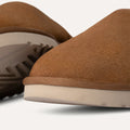 Close-up of two tan Ugg M Classic Slip-On slippers showcasing luxurious UGGplush™ lining and thick white rubber soles on a white background.