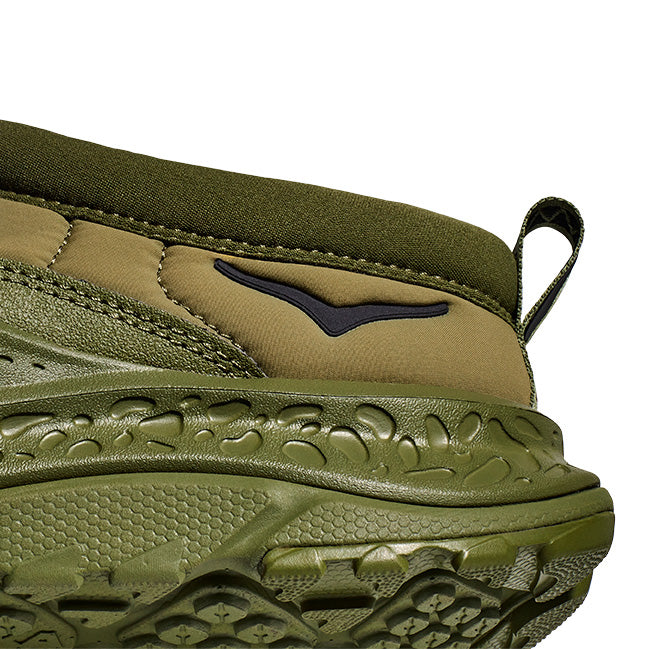 Close-up of the Hoka U Ora Primo in green: a slip-on shoe featuring a textured sole, dark green upper, and black chevron logo. Ideal for lifestyle comfort and effortless style.