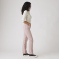 A person stands in profile against a plain background, wearing a white long-sleeve top, Levis 501 Original jeans in Scraped Pale Mauve, and black sneakers.