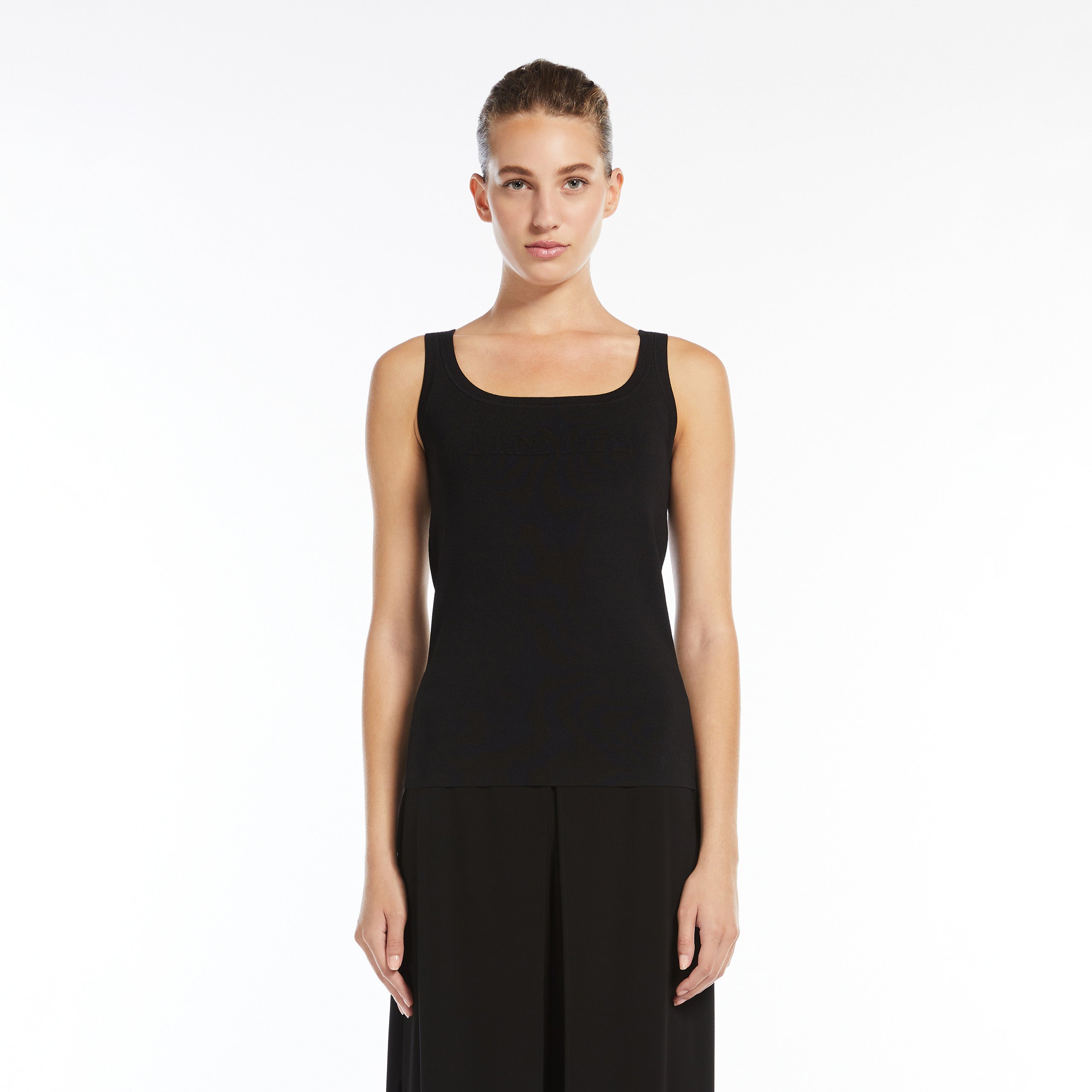 A woman with hair pulled back stands facing forward, wearing the Max Mara Pentola Sweater Tank Top and black viscose crêpe yarn pants against a plain white background.