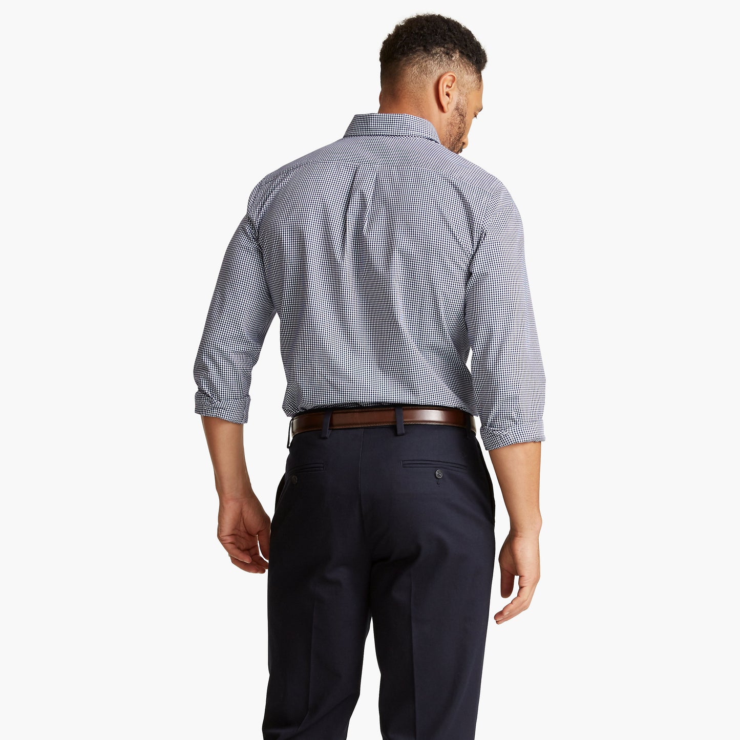 A man faces away, wearing a Dockers Men's Signature Comfort Flex Shirt, LS with rolled-up sleeves and dark trousers with a brown belt, against a plain white background.