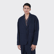 A man stands facing forward against a plain light gray background, wearing Kardo’s Hugh 2.0 Blazer in Blue Black Stripe over a patterned shirt.
