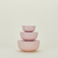 The Essential Lidded Bowls set by Hawkins New York features three stackable pink bowls in varying sizes, crafted from recycled bamboo, displayed neatly against a beige background.