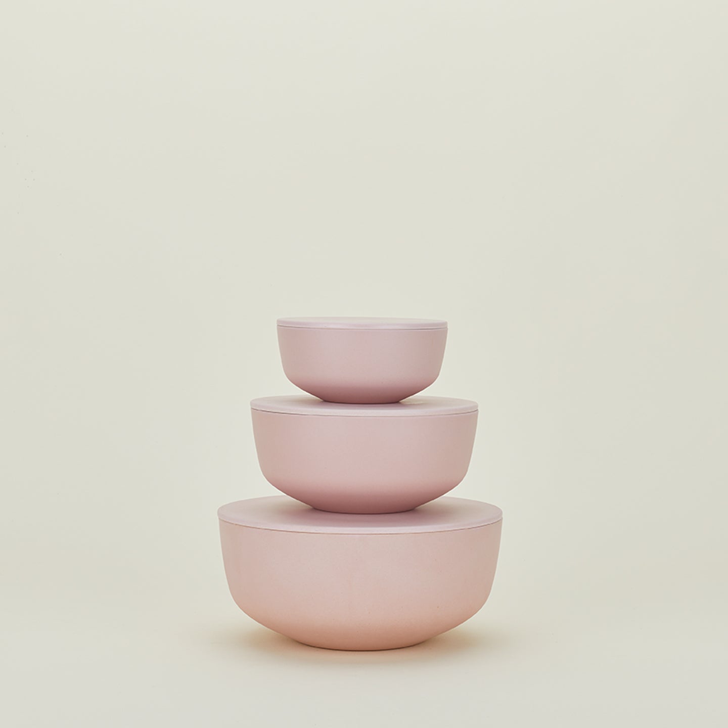 The Essential Lidded Bowls set by Hawkins New York features three stackable pink bowls in varying sizes, crafted from recycled bamboo, displayed neatly against a beige background.