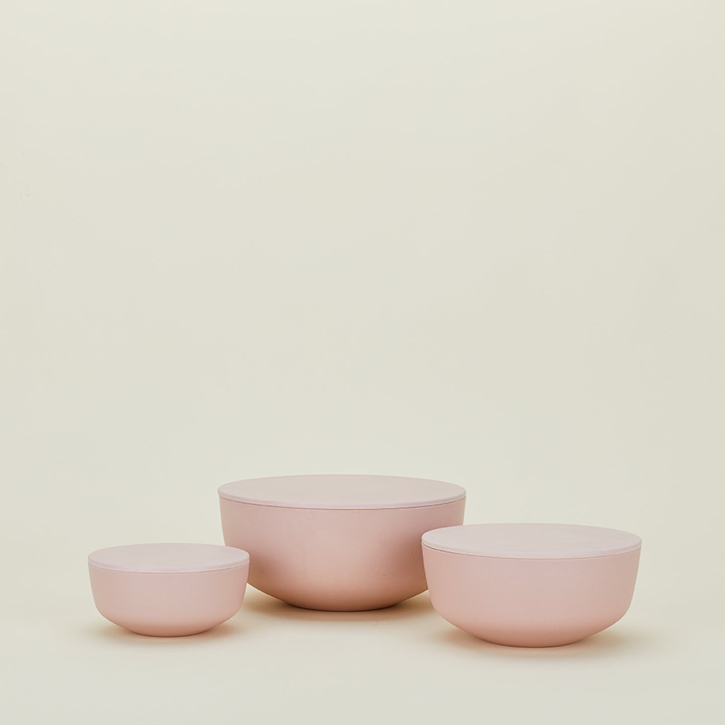 The Hawkins New York Essential Lidded Bowls, a set of three in pink ceramic and crafted for perfect stackability, are arranged against a plain cream background.