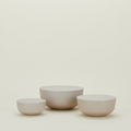 The "Essential Lidded Bowls" set of three beige ceramic bowls by Hawkins New York, designed for stackable storage, is arranged on a plain, light background.