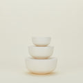 A set of three nestable, off-white ceramic bowls called "Essential Lidded Bowls" by Hawkins New York, are stacked against a plain light background.