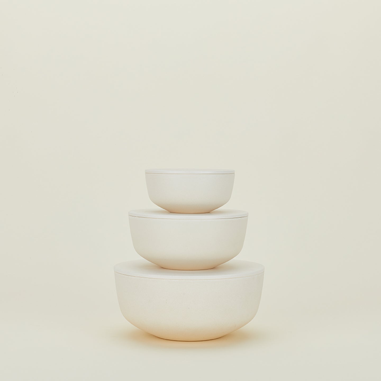 A set of three nestable, off-white ceramic bowls called "Essential Lidded Bowls" by Hawkins New York, are stacked against a plain light background.