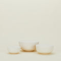 Hawkins New York's Essential Lidded Bowls, a set of three off-white ceramic bowls in varying sizes, rest beautifully on a neutral background. Their stackable design offers functionality and elegance, making them a stylish addition to any kitchen décor.