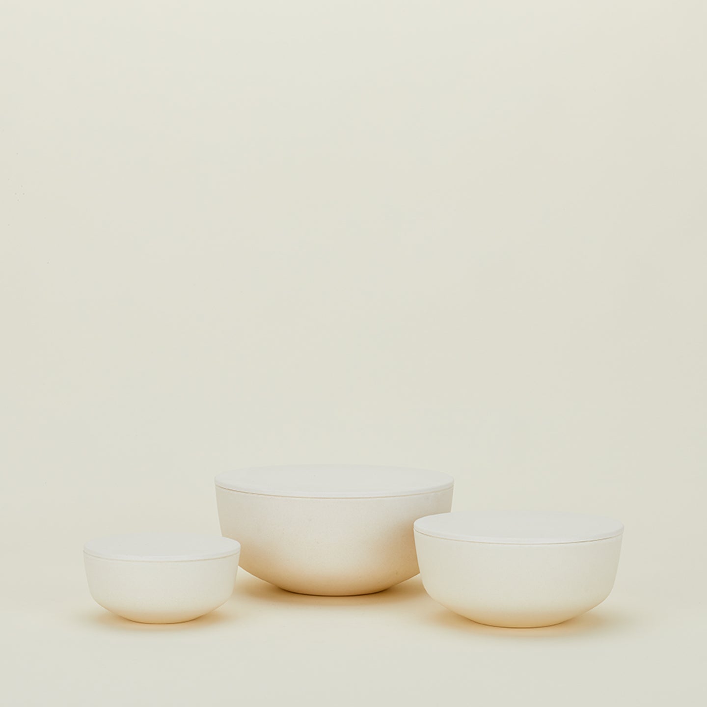 Hawkins New York's Essential Lidded Bowls, a set of three off-white ceramic bowls in varying sizes, rest beautifully on a neutral background. Their stackable design offers functionality and elegance, making them a stylish addition to any kitchen décor.