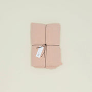The Simple Linen Fitted Sheet - Queen by Hawkins New York, crafted from pink European linen with a stonewashed texture, is folded and tied with black string and marked by a white tag. It rests elegantly on a light surface, highlighting its quality woven in Portugal.