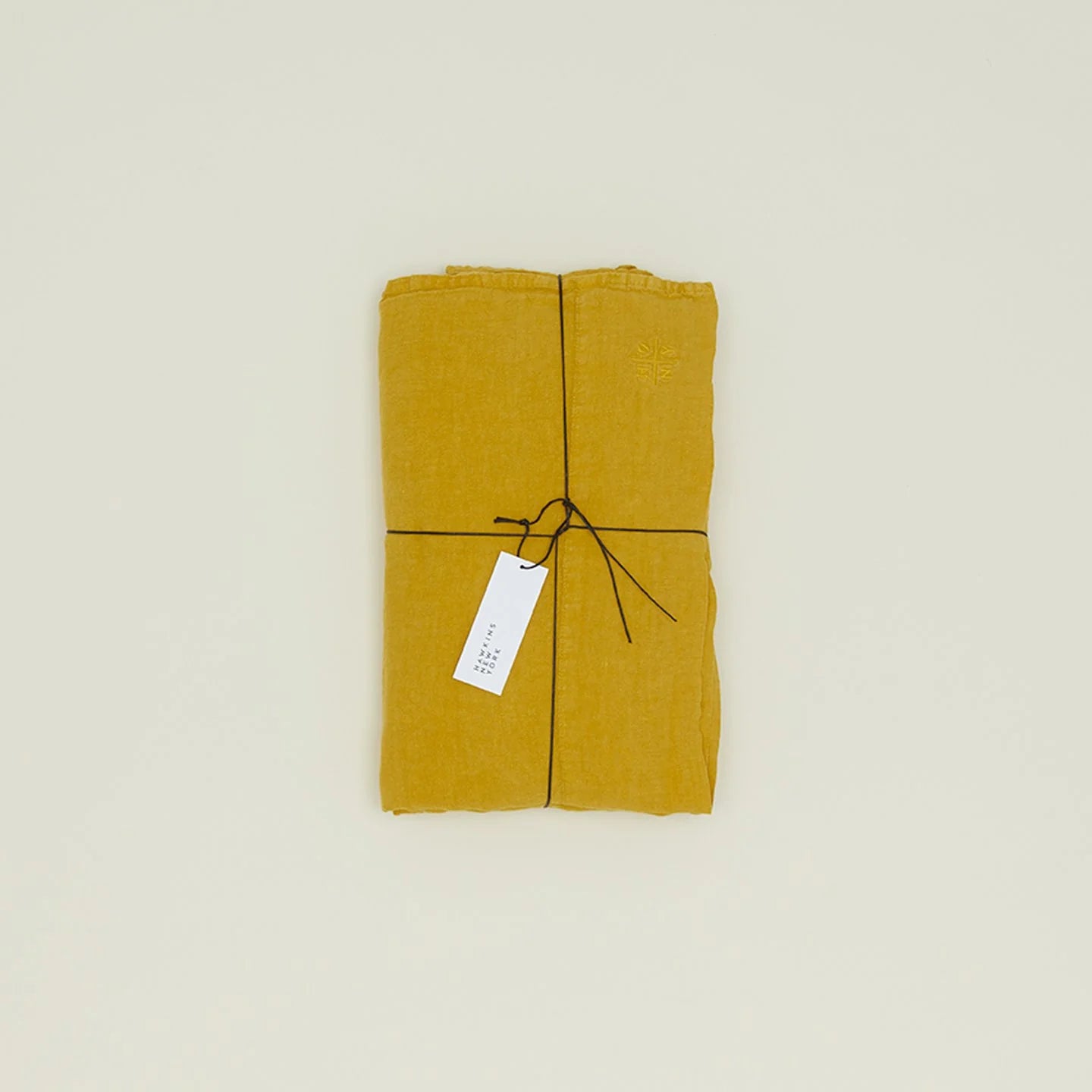 A folded mustard yellow Simple Linen Bedding - Queen Flat Sheet by Hawkins New York, tied with black string and a small white tag, rests on a plain light background.