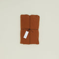 A folded brown Simple Linen Fitted Sheet by Hawkins New York, tied with black string and a white tag attached, rests elegantly on a light background.