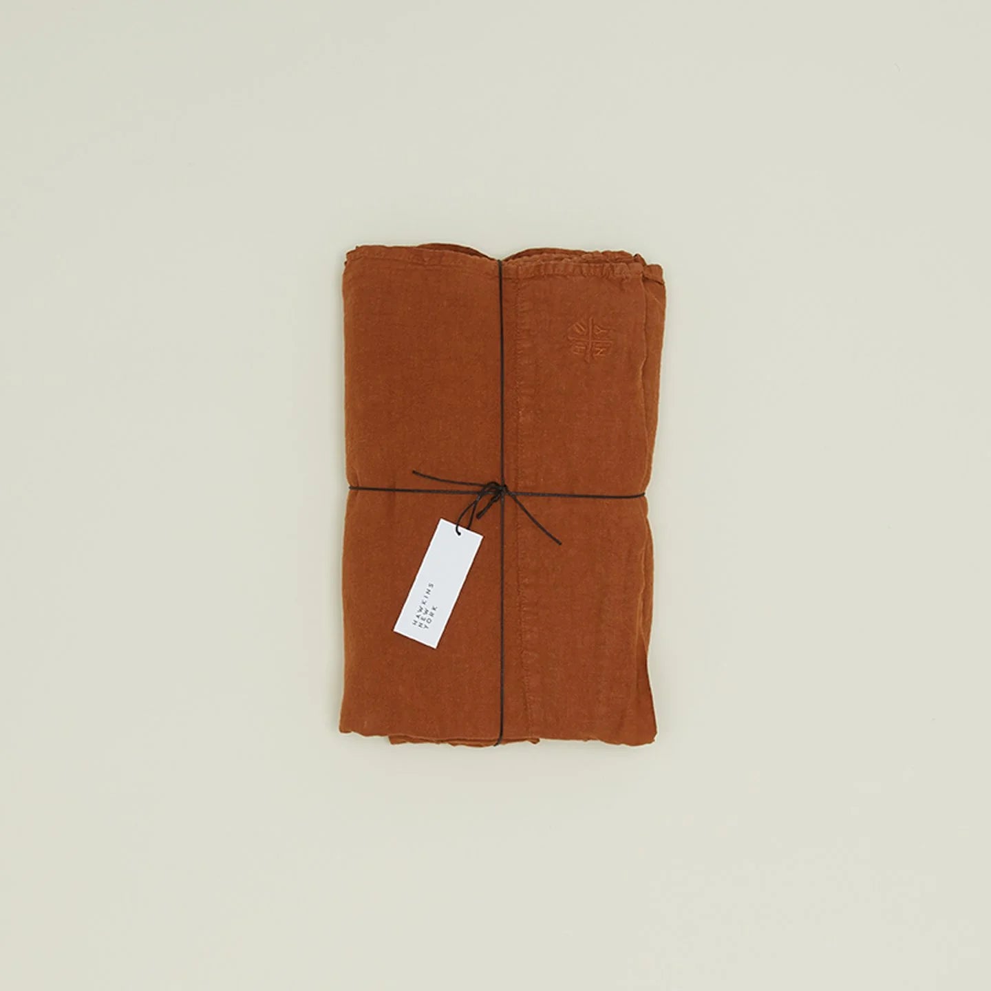 A folded brown Simple Linen Fitted Sheet by Hawkins New York, tied with black string and a white tag attached, rests elegantly on a light background.