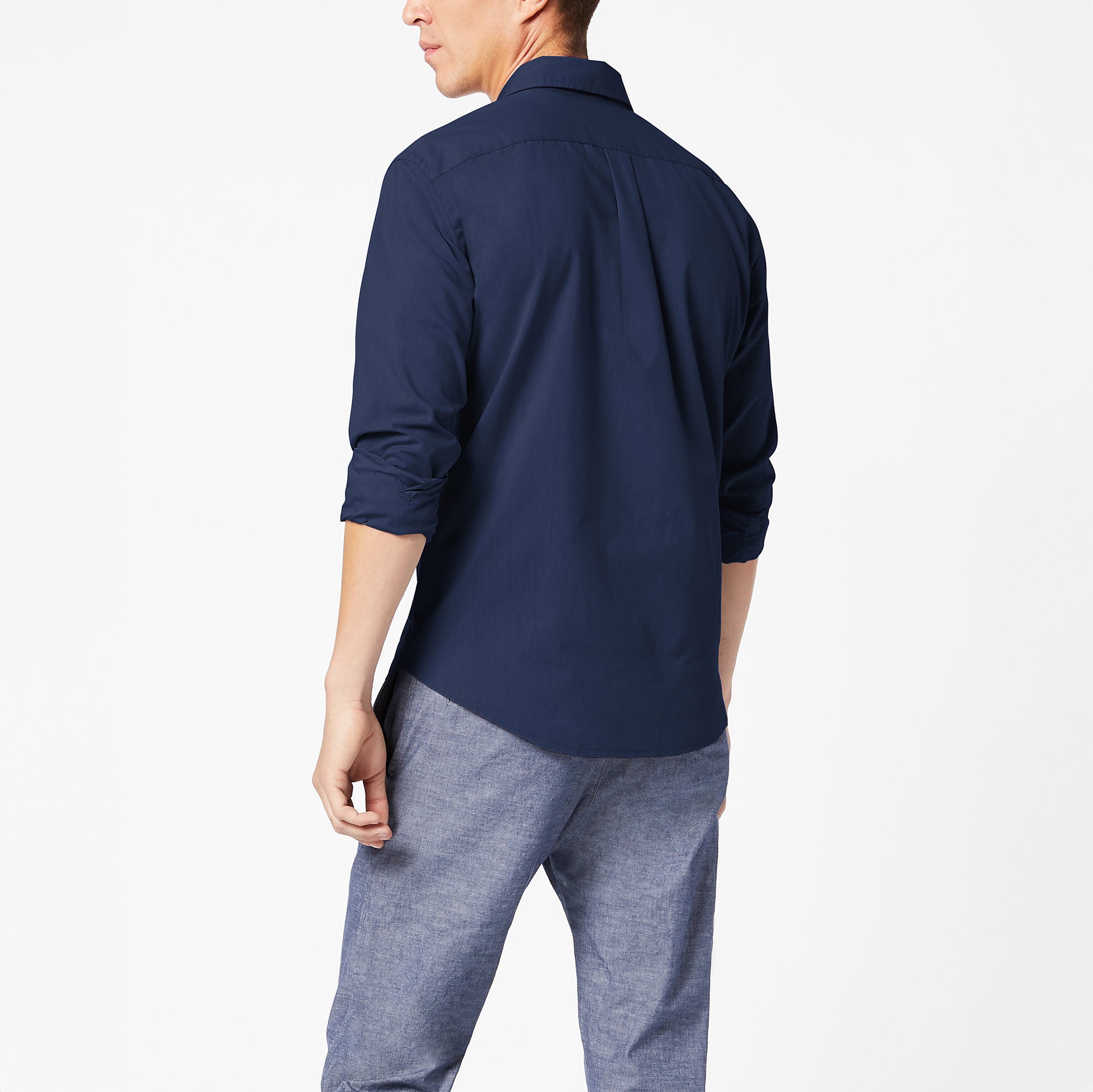 A person stands with their back to the camera, wearing a Dockers Men's Signature Comfort Flex Shirt, LS in navy blue and gray pants against a plain white background.