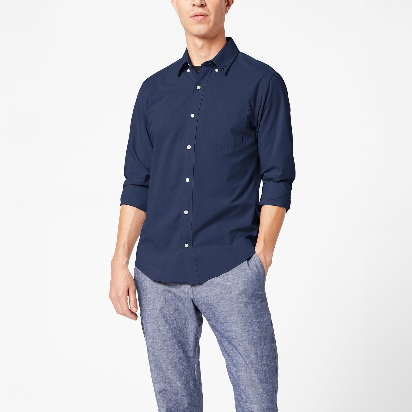 A man wears a Dockers Men's Signature Comfort Flex Shirt, LS in navy blue with rolled sleeves and light gray pants, standing against a plain white background.