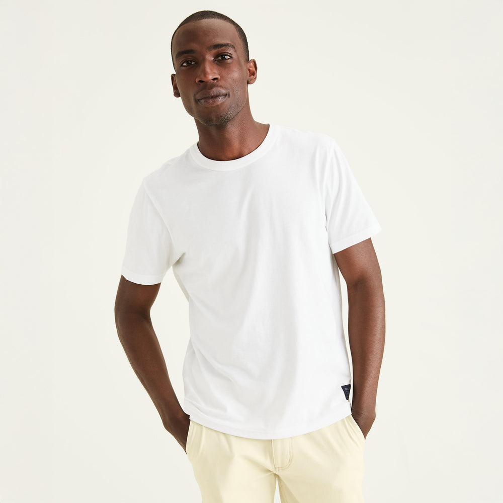 A man stands against a light background with his hands in his pockets, wearing the Dockers Men's Crewneck Tee and light-colored pants.
