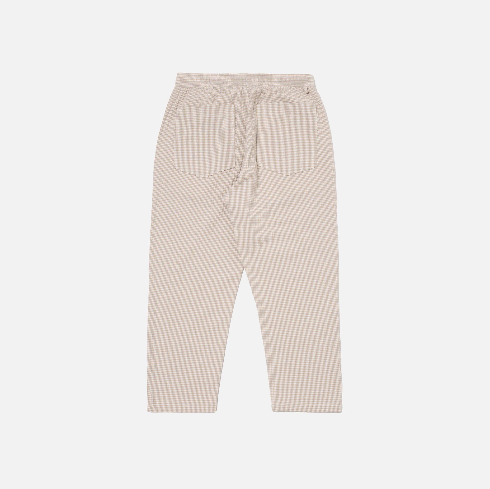 The Universal Works Ospina Check Cotton High Water Trouser in Ecru/Sand is shown flat from the back, highlighting its textured fabric, elastic waistband, and two rear patch pockets.