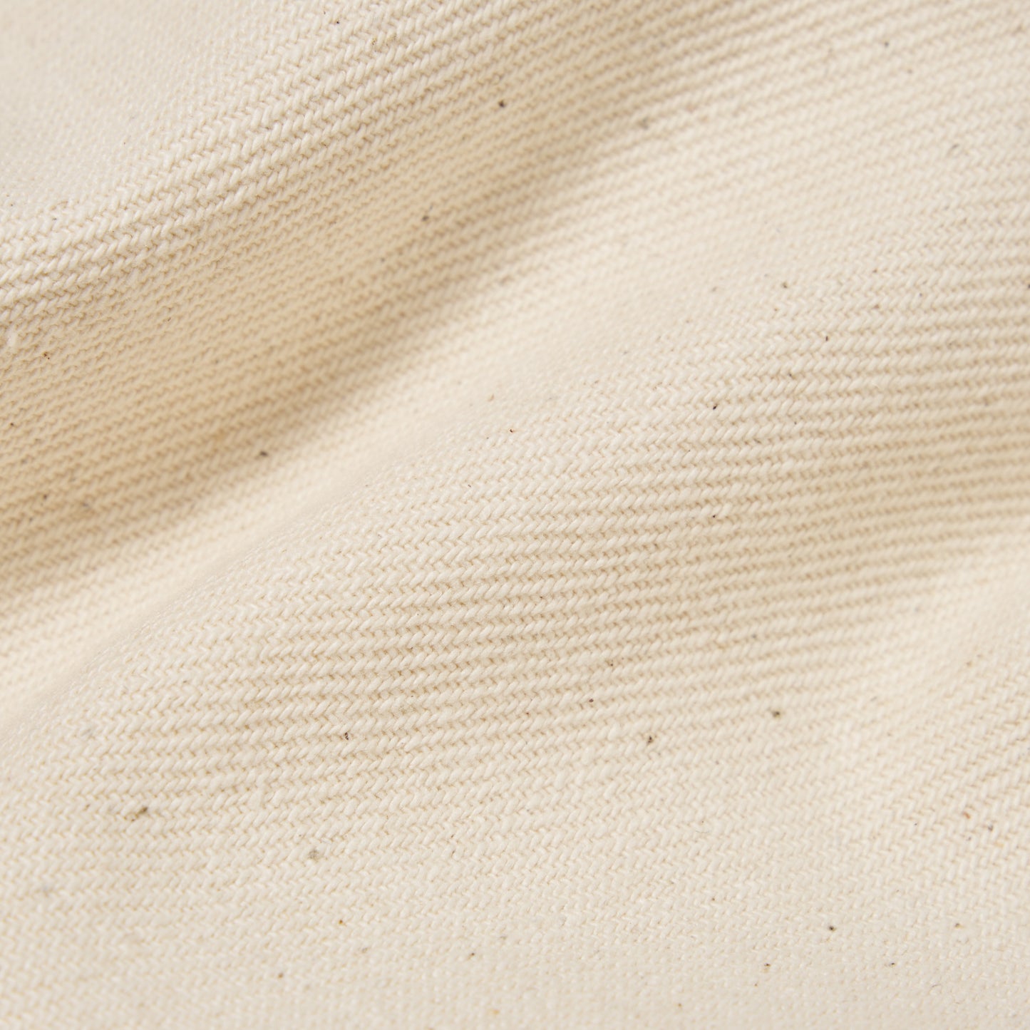 Close-up of the Universal Works Recycled Cotton Duke Pant in Ecru, showing beige woven fabric with a visible textured pattern, small dark specks, and slight wrinkling.