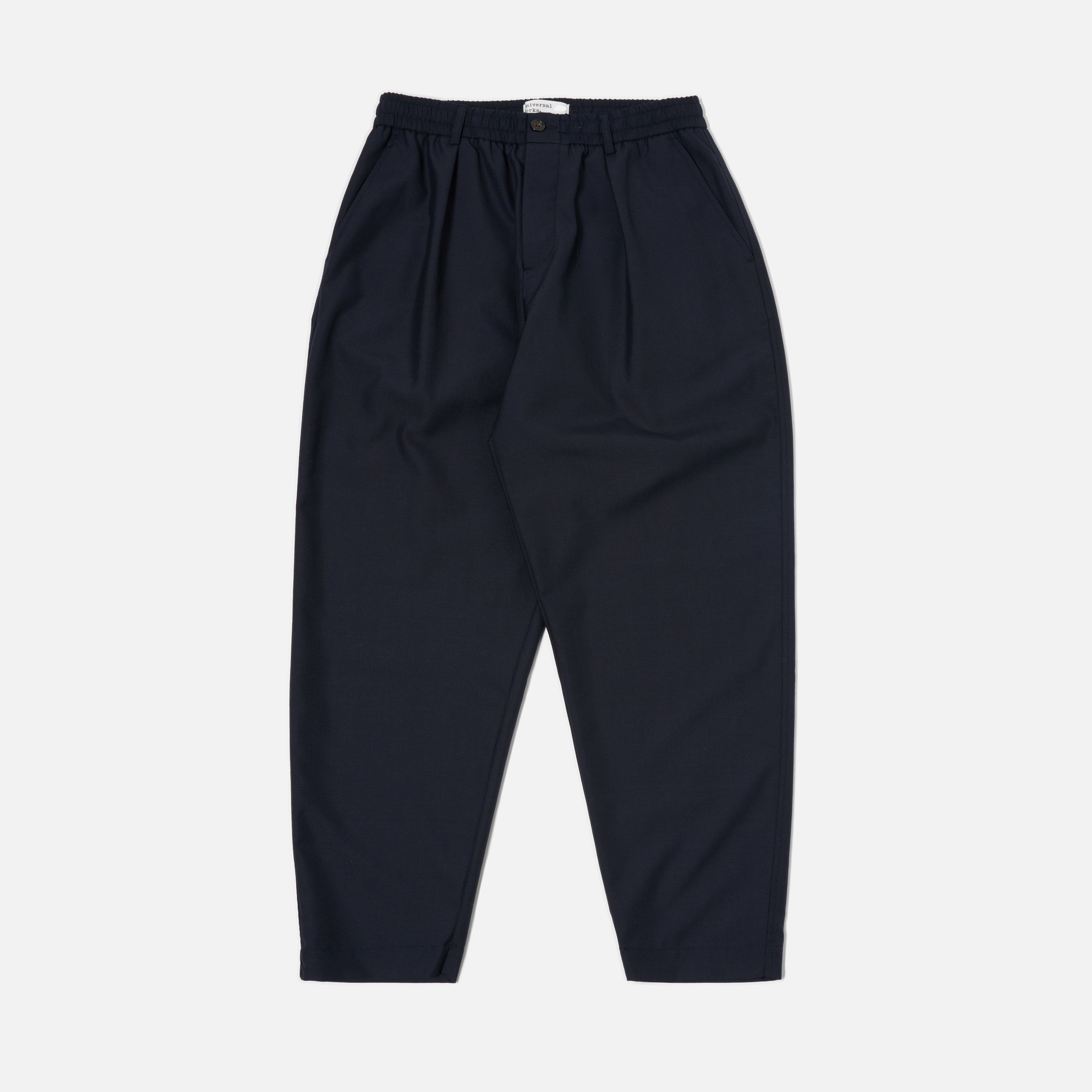 The Universal Works Tropical Suiting Pleated Track Pant in navy features a high waist, pleats, and an elastic waistband, shown flat on a white background.