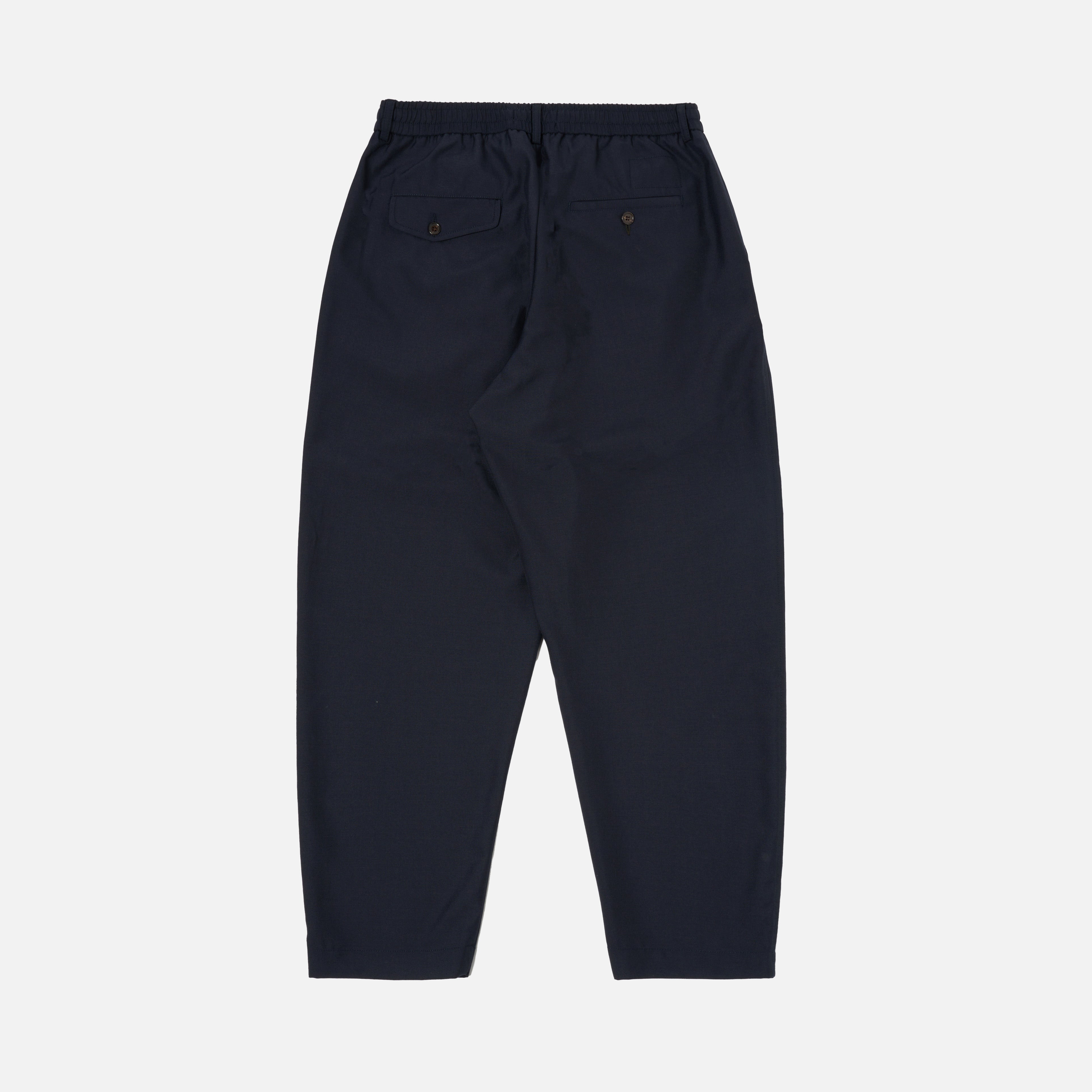 The Universal Works Tropical Suiting Pleated Track Pant in navy features an elastic waistband and two back pockets, displayed flat on a white background.