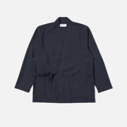 The Universal Works Tropical Suiting Kyoto Work Jacket in navy features long sleeves, a waist tie, and three front pockets, displayed flat on a white background.