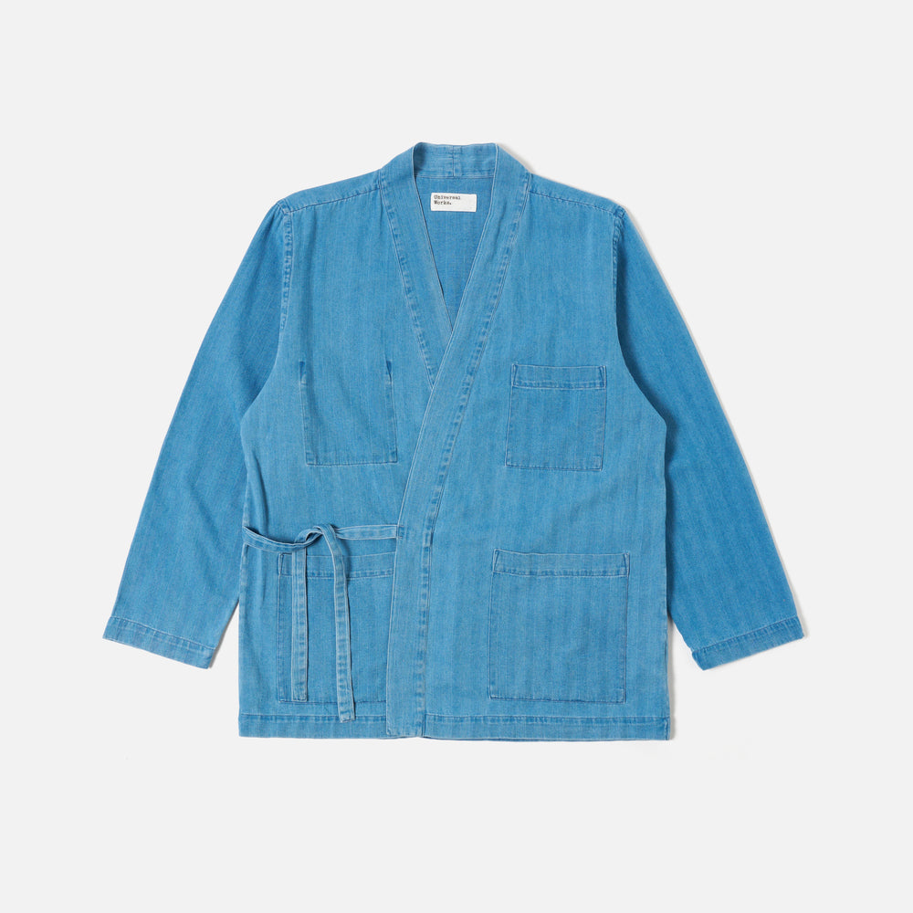 The Universal Works Herringbone Recycled Kyoto Work Jacket in Washed Indigo features long sleeves, an open front, self-tie belt, and three patch pockets, displayed flat on a white background.