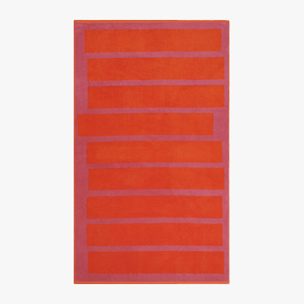 The Stack Towel by Lateral Objects is a rectangular rug with horizontal red-orange stripes on a purple background, made from plush velour towel fabric for a soft and stylish accent.