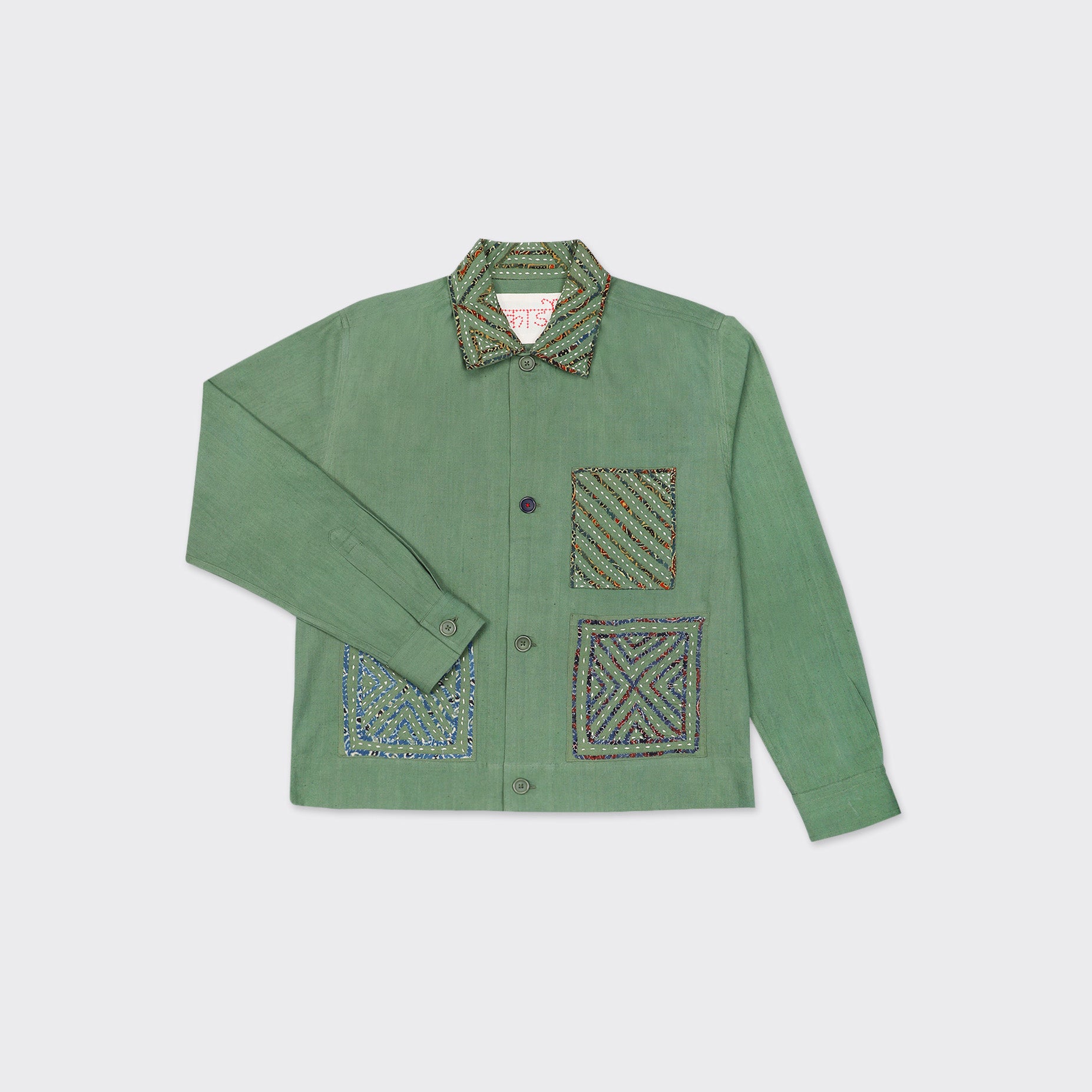 The Kardo Bodhi Jacket in Matcha Rabari Applique features a green button-up design with a collar, three patterned fabric patches on the front, and one patch on the collar.