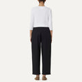 Rear view of a person wearing a white cotton poplin long-sleeve shirt and Panta Vela Pant, Clara by Labo Art, standing barefoot on a light background.