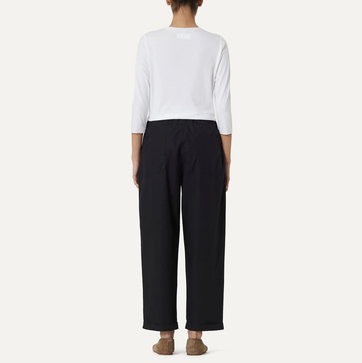 Rear view of a person wearing a white cotton poplin long-sleeve shirt and Panta Vela Pant, Clara by Labo Art, standing barefoot on a light background.