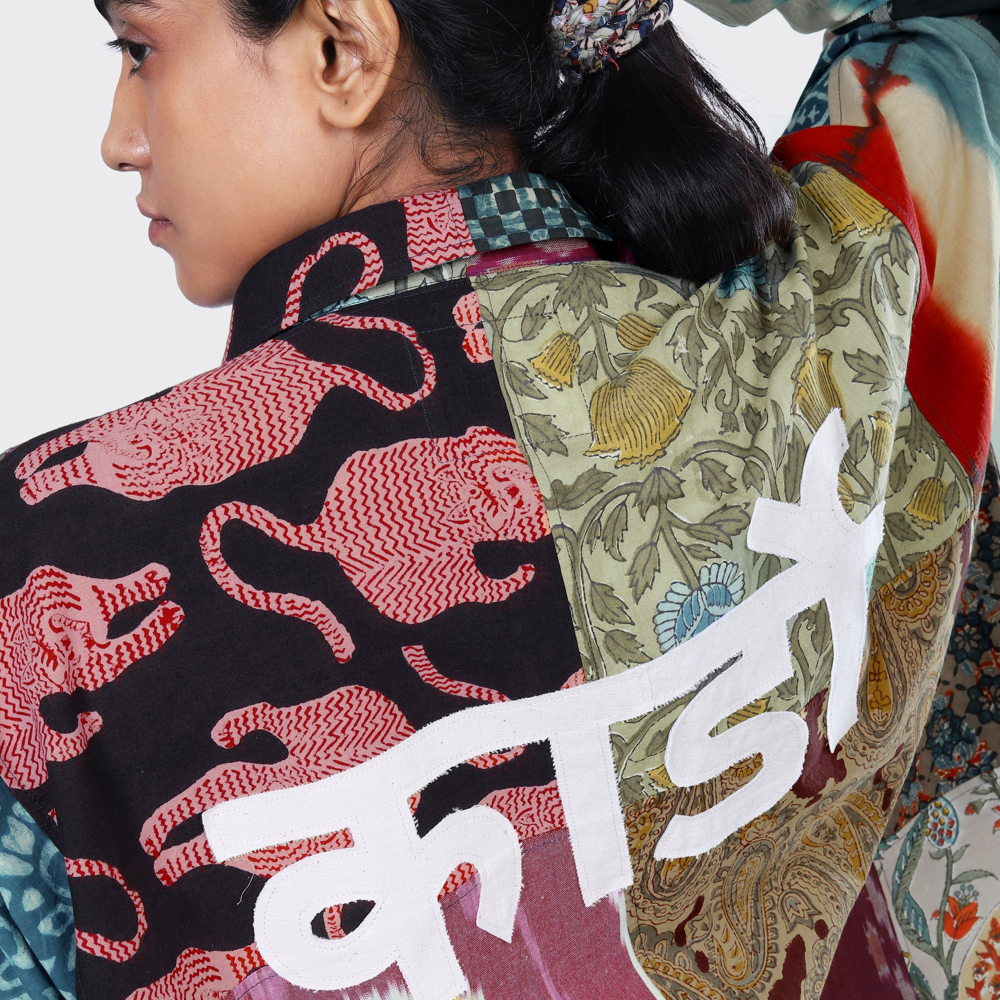 A person in Kardo’s Fanette Overshirt, Patchwork 07—a vibrant red, black, and green patchwork piece featuring select fabrics and bold white Hindi script painted on the back.