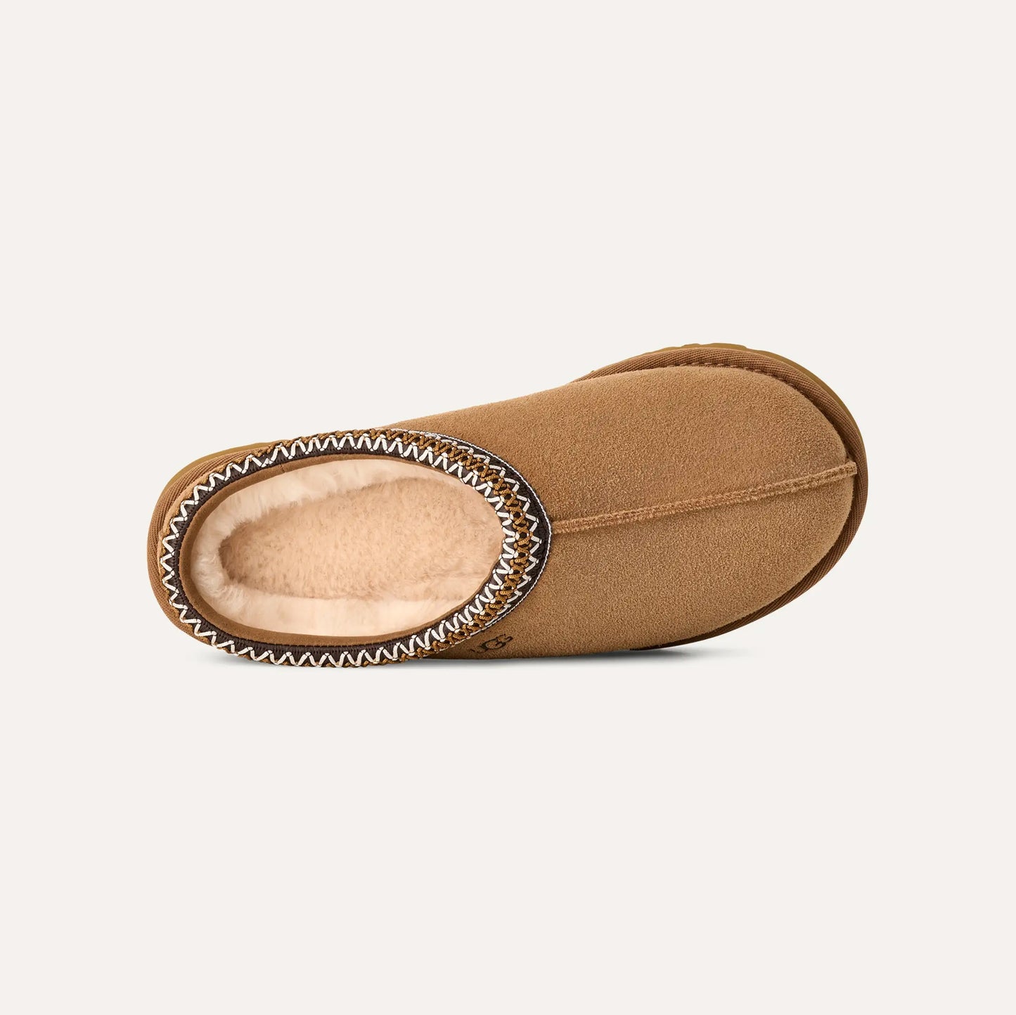 The W's Tasman by Ugg is presented as a single brown suede slipper featuring visible stitching. Its slip-on silhouette and cozy UGGplush™ lining are showcased against a white background.