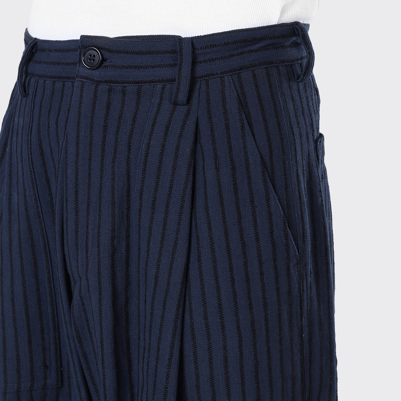 Close-up of a person wearing Kardo’s Yuki Pleated Trousers in Blue Black Stripe, featuring a button and waistband detail, with one hand in the pocket.