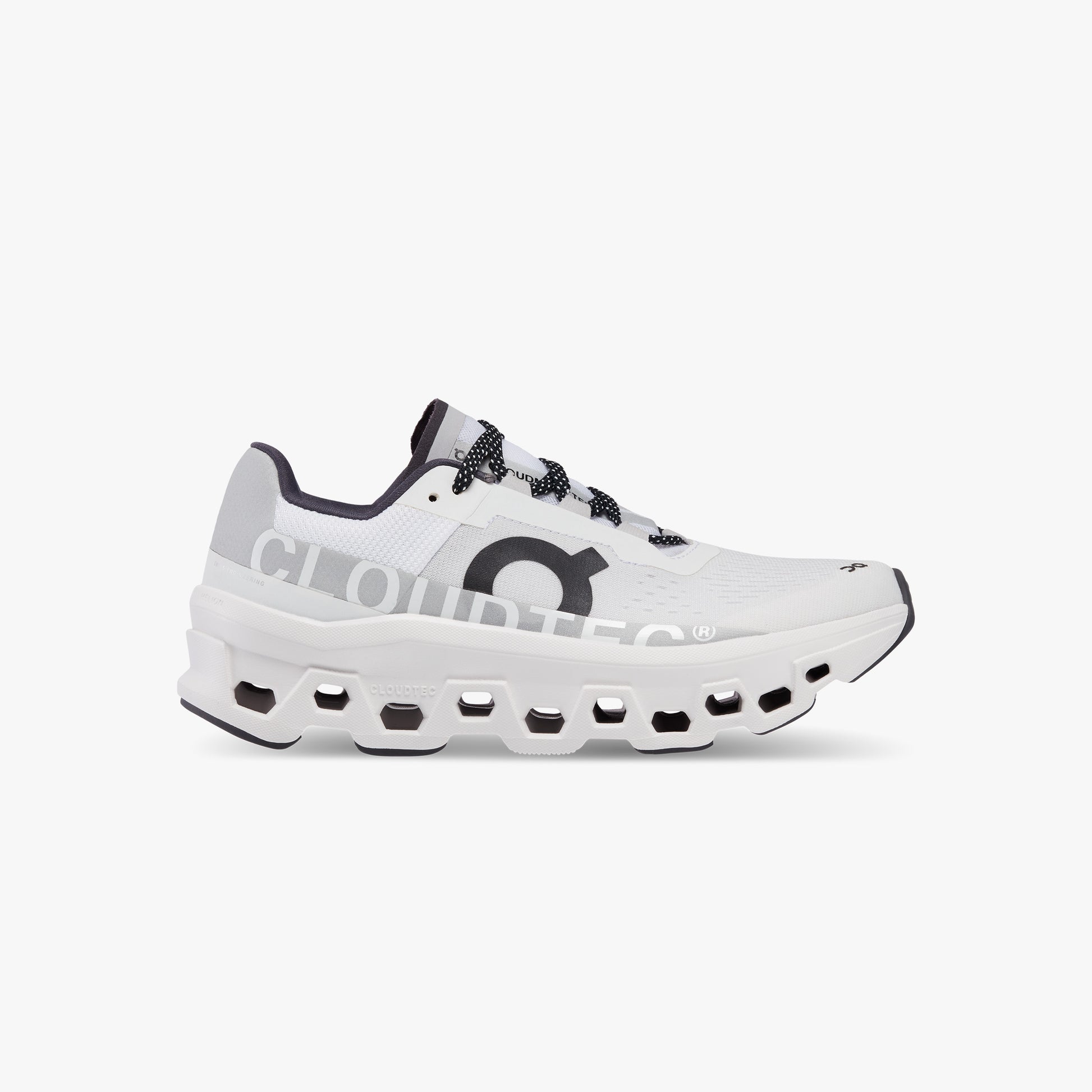 The On Running M Cloudmonster, All White, is a white athletic running shoe with black and gray accents, a chunky segmented sole marked "CLOUDTEC," and Helion™ superfoam for ultra-cushioned comfort on every run.
