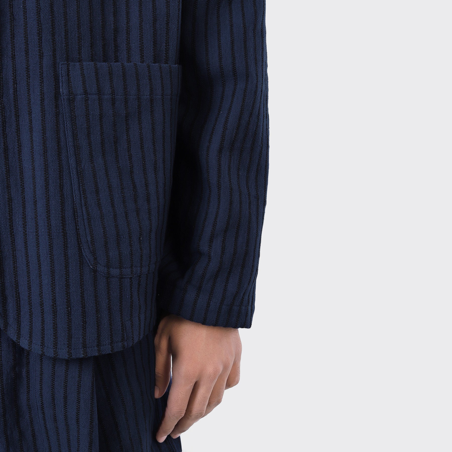 A person models the Kardo Hugh 2.0 Blazer in Blue Black Stripe, featuring vertical stripes and a front pocket. The image captures the lower half of the jacket and their right hand against a plain background.