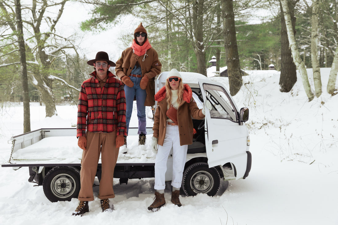 Three Four people standing in front of a small white truck in a snowy forest.