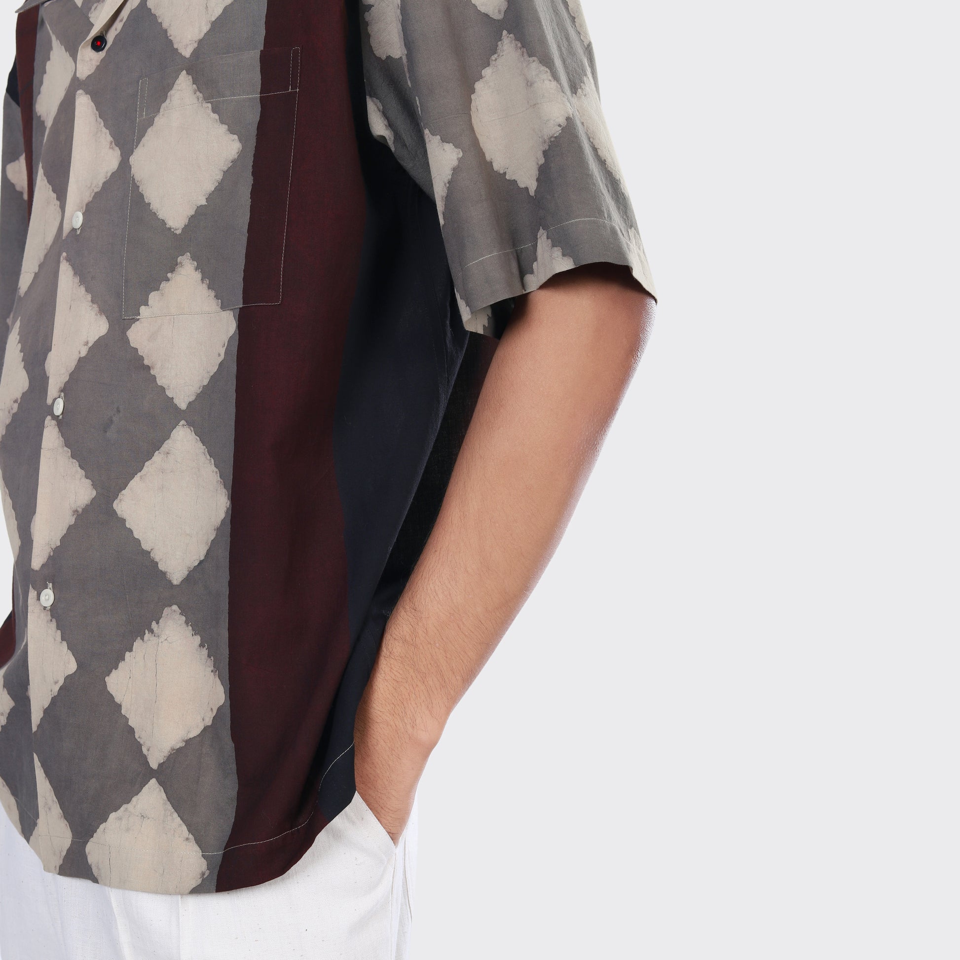 A person wearing the Kardo Rohit Shirt, Block Print 139—a short-sleeved button-up with a geometric diamond pattern—paired with white pants, shown from the side against a plain background.