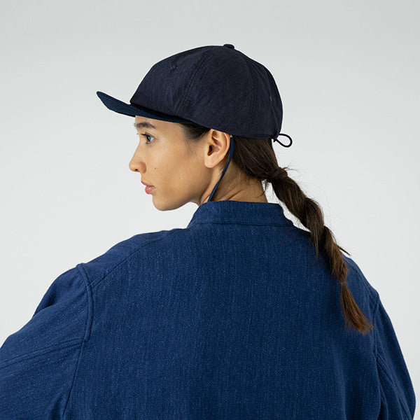 A person with a braid, wearing the Sublime Roe Charidoor Cap and a matching denim jacket, is seen from the back and side against a plain light background.